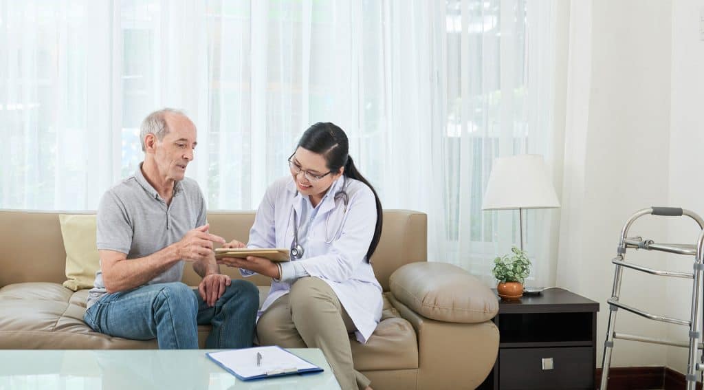 A nurse is talking to an elderly man on a couch.
