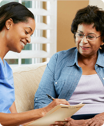A nurse sitting on a couch talking to an older woman.